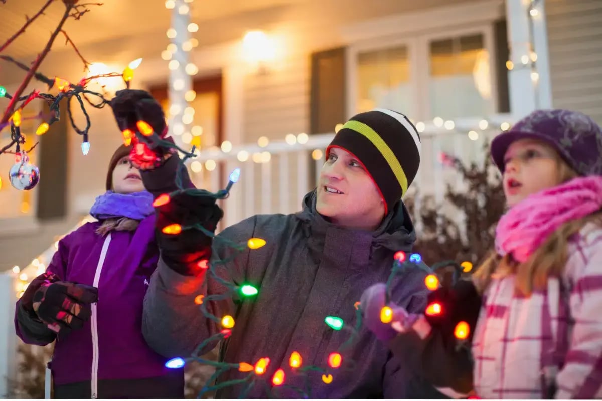 family hanging lights outside in tree following Christmas light safety